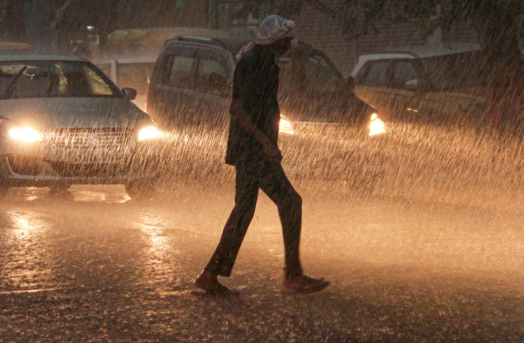 A man crosses a road amid rainfall, in Gurugram. (Photo: PTI)