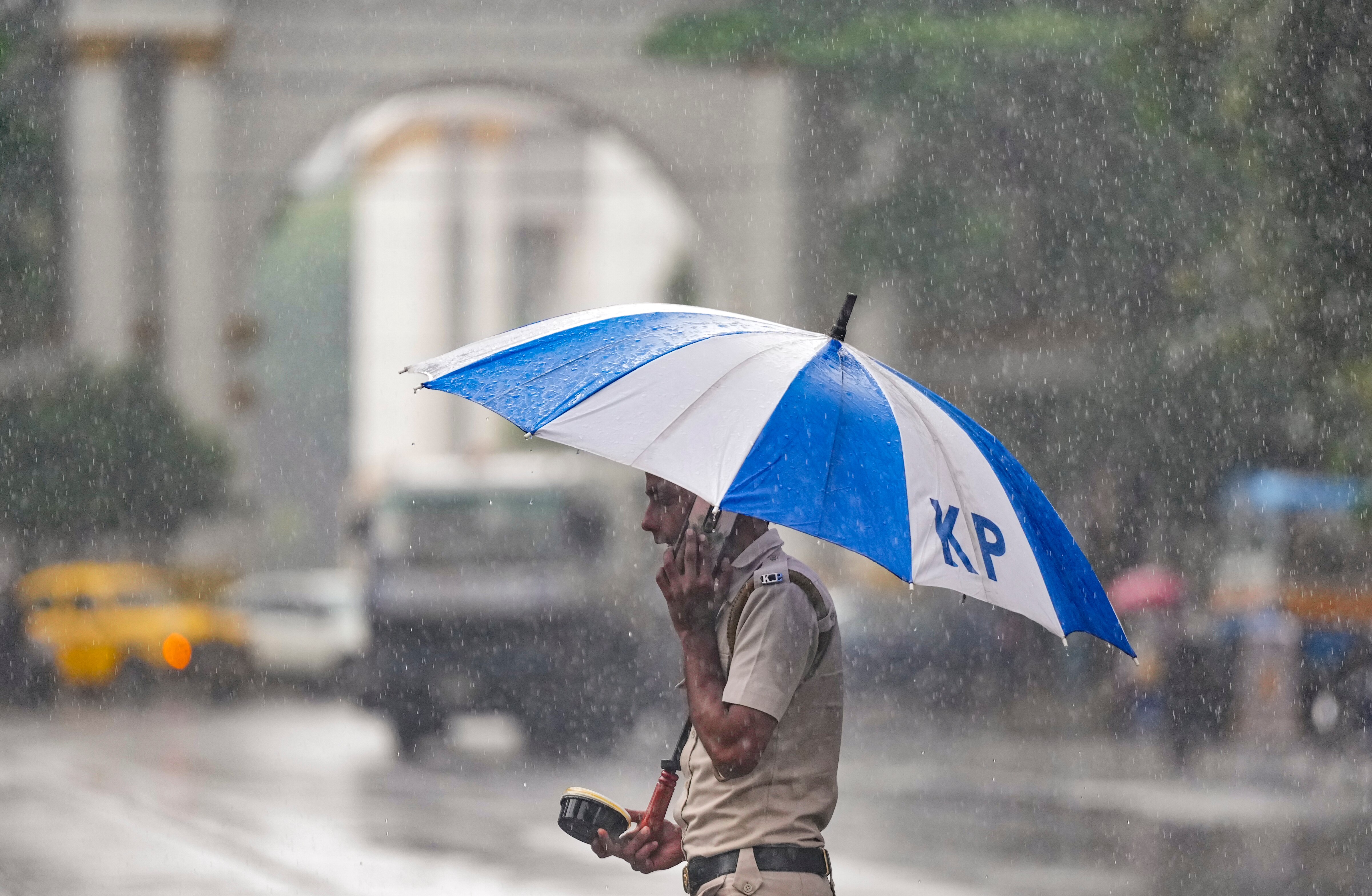 A police personnel shields himself amid rainfall. (Photo: PTI)