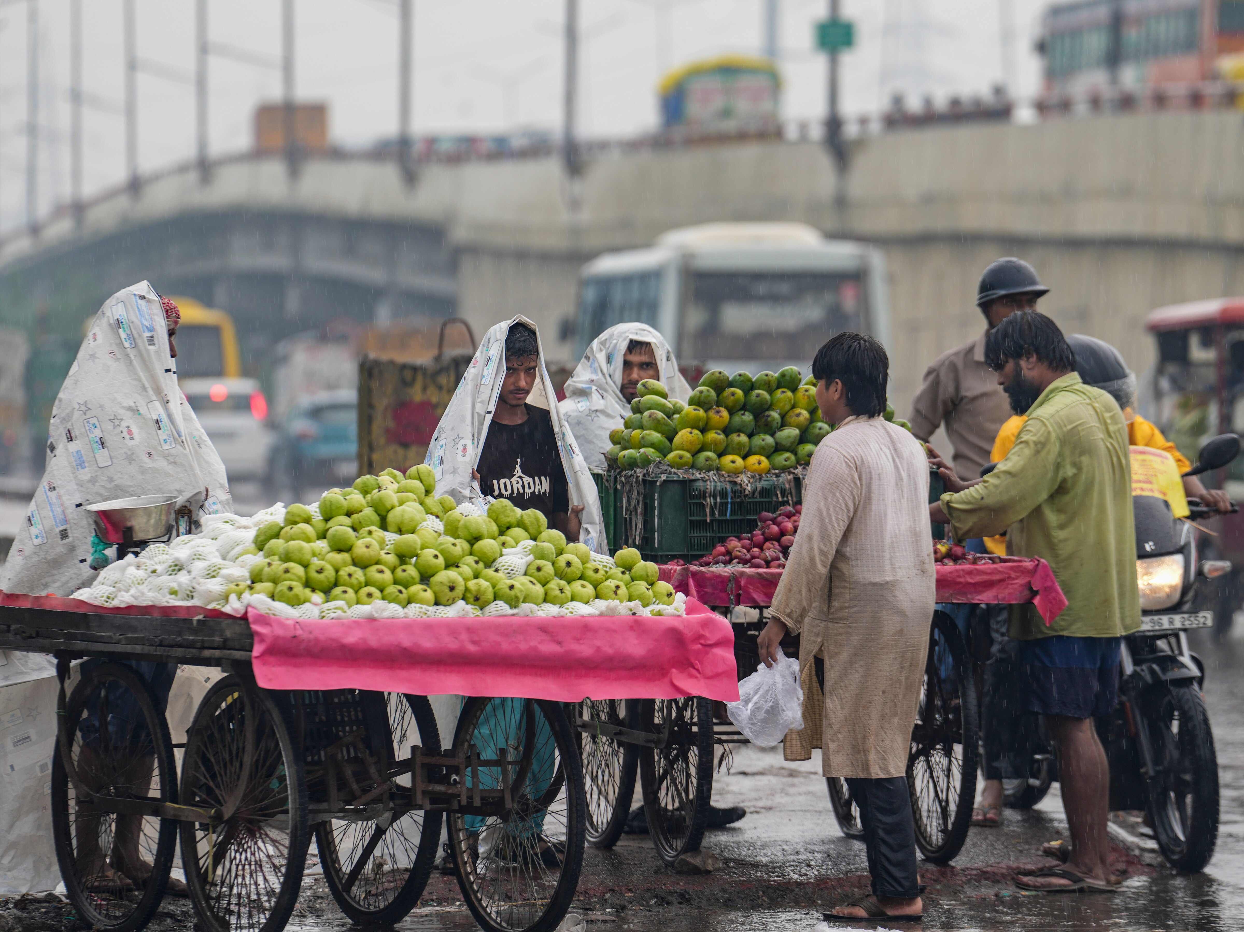 Fruit vendors cover themselves with plastic sheets as attend to customers amid rain in New Delhi. (Photo: PTI)
