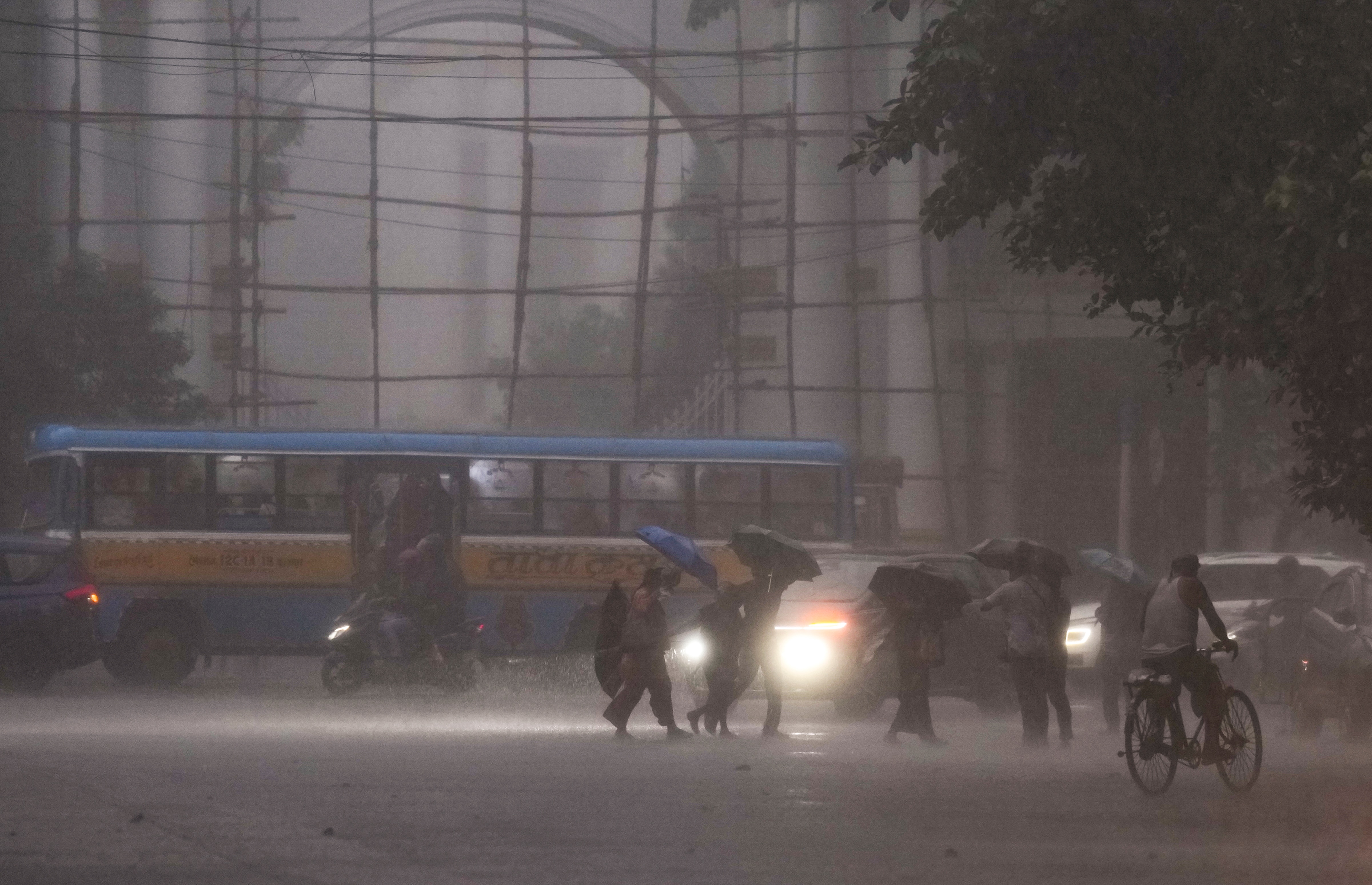 Vehicles move with headlights on as pedestrians wade through a road during heavy rain. (Photo: PTI)