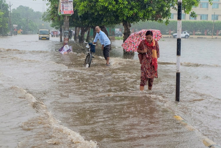 People wade through a waterlogged road amid heavy rain, in Gurugram. (Photo: PTI)
