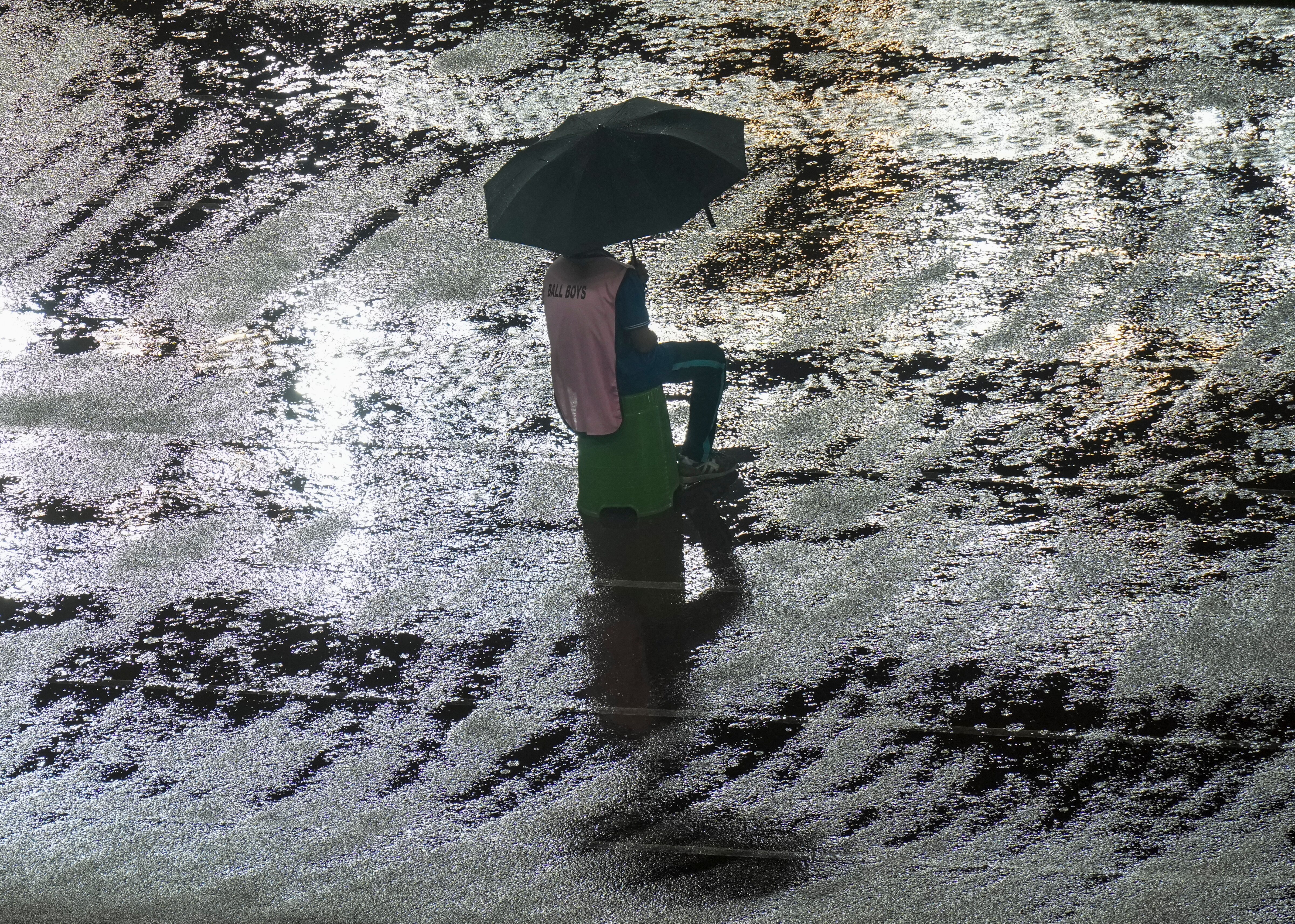 A ball boy sits under an umbrella on a stool amidst heavy rain. (Photo: PTI)