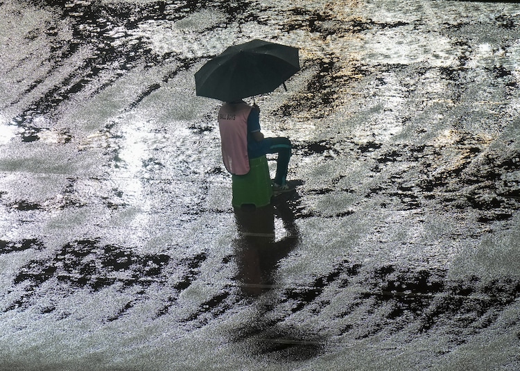A ball boy sits under an umbrella on a stool amidst heavy rain. (Photo: PTI)