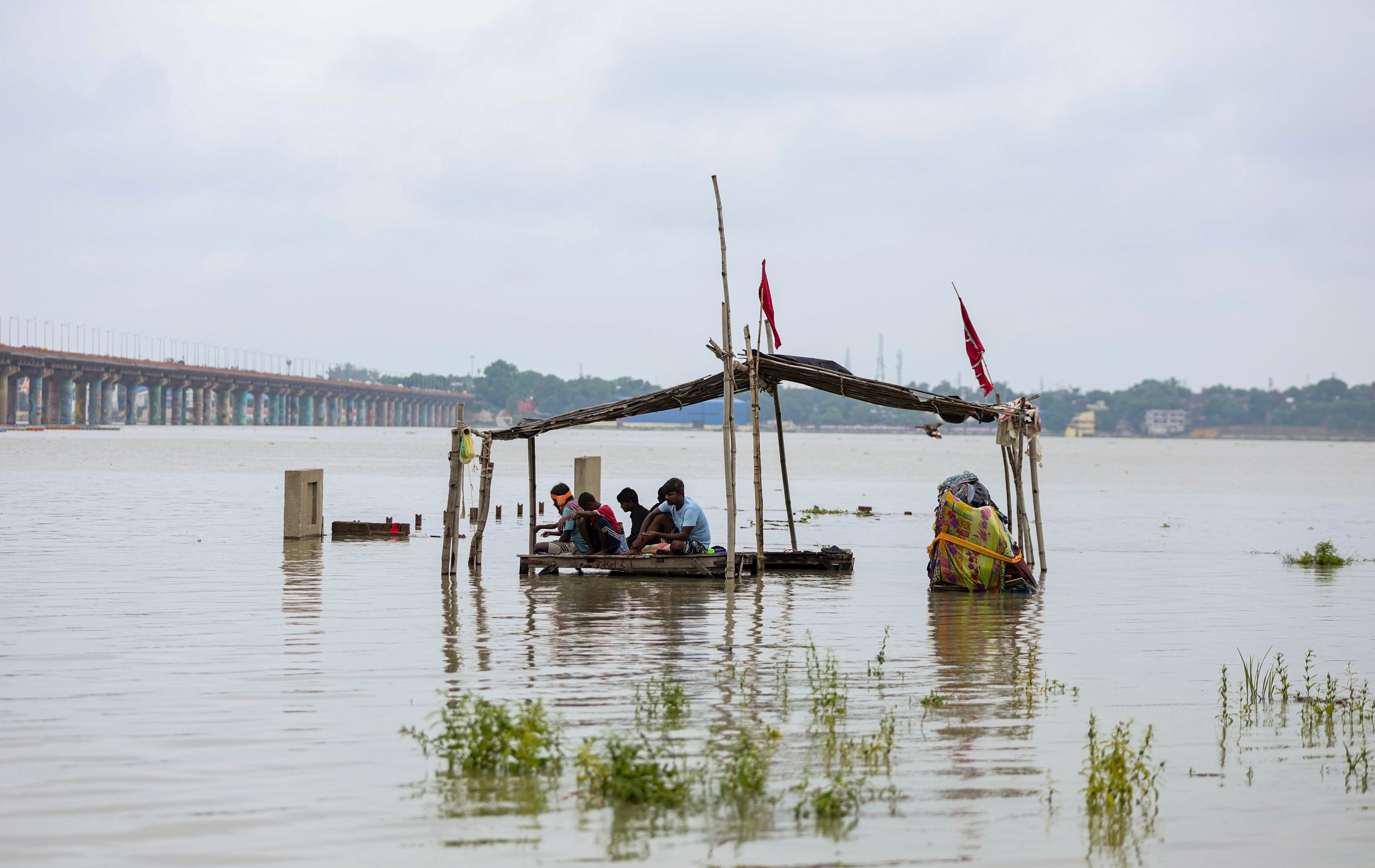 People sit on a partially submerged wooden platform after heavy rain. (Photo: PTI)
