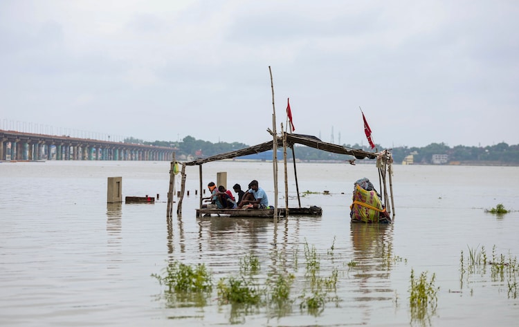 People sit on a partially submerged wooden platform after heavy rain. (Photo: PTI)