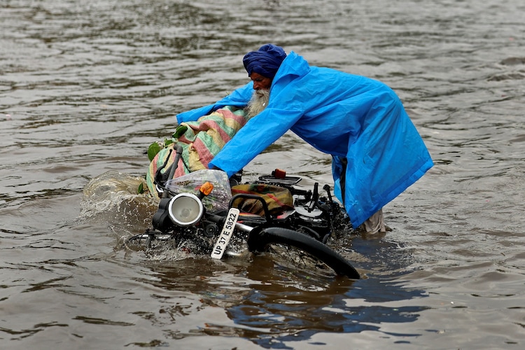 A man picks up his motorbike from a waterlogged street amid rain in New Delhi. (Photo: PTI)