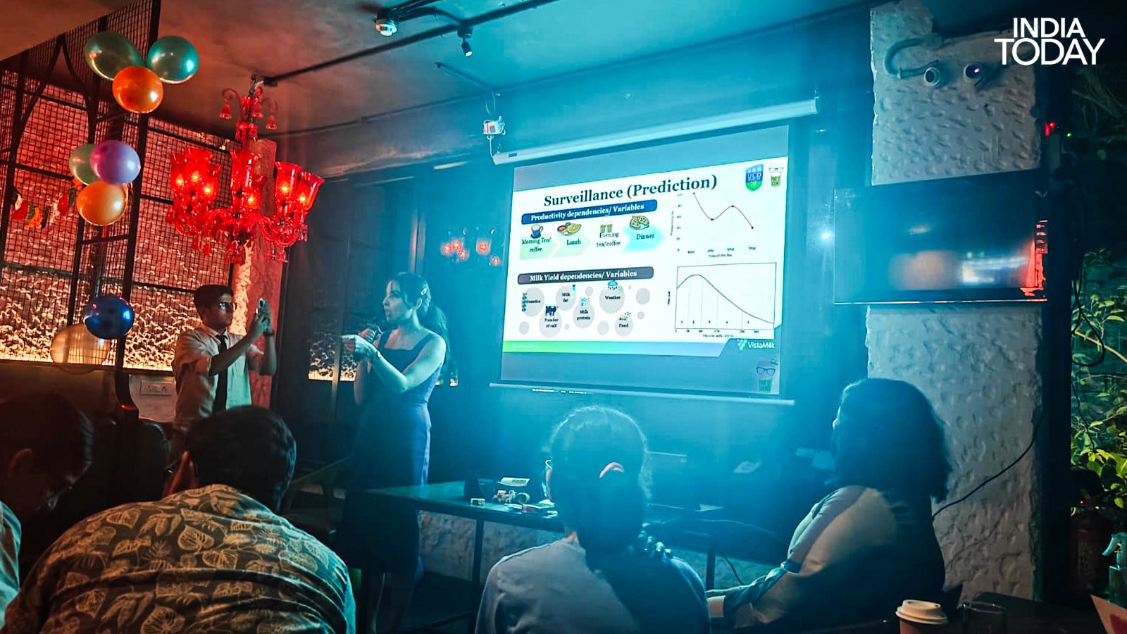 Dr Pratiksha Nagar presenting her surveillance and prediction framework at Pint of Science 2026, Delhi. The slide shows milk yield curves alongside human productivity data. Deviations in a cow's 305-day lactation cycle, she explained, can signal an incoming disease long before any symptom appears in a human population. (Photo: Radifah Kabir/India Today)