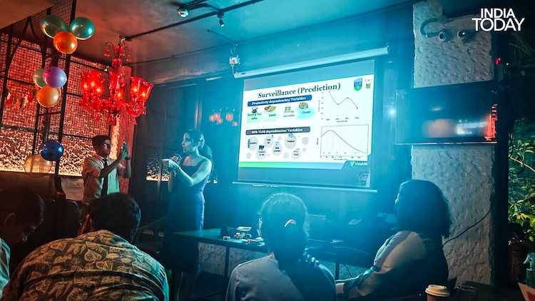 Dr Pratiksha Nagar presenting her surveillance and prediction framework at Pint of Science 2026, Delhi. The slide shows milk yield curves alongside human productivity data. Deviations in a cow's 305-day lactation cycle, she explained, can signal an incoming disease long before any symptom appears in a human population. (Photo: Radifah Kabir/India Today)