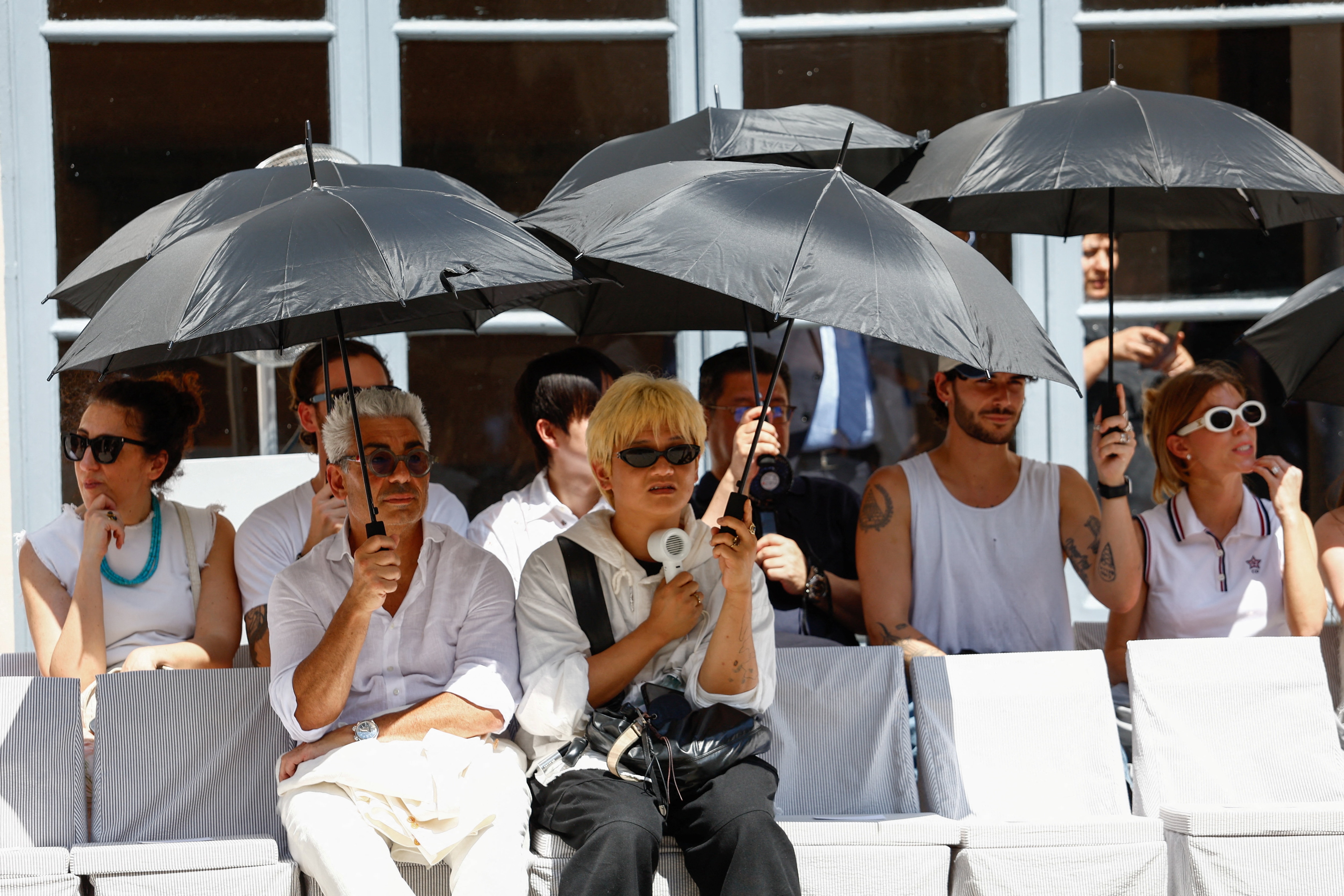 People shield themselves with umbrellas from the sun during Thom Browneâs Spring/Summer 2027 menâs collection show in Milan, Italy. 