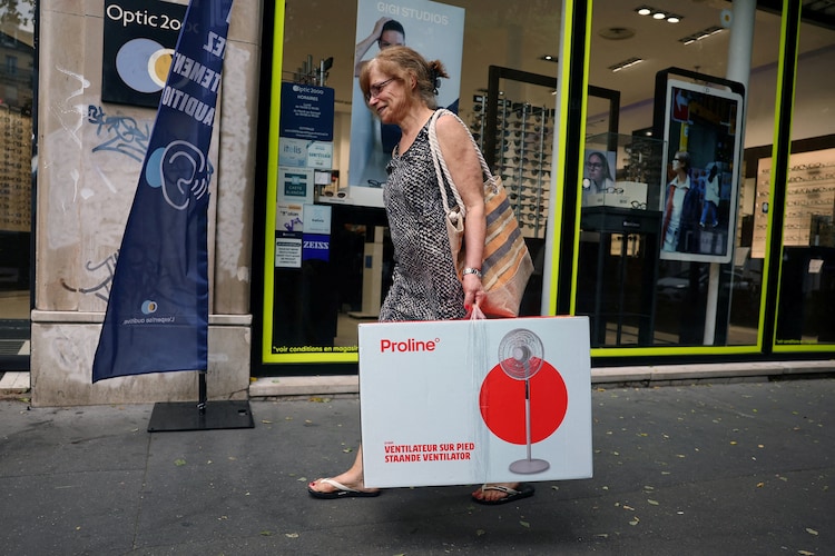 A woman carrying an electric fan in a cardboard box walks down a street