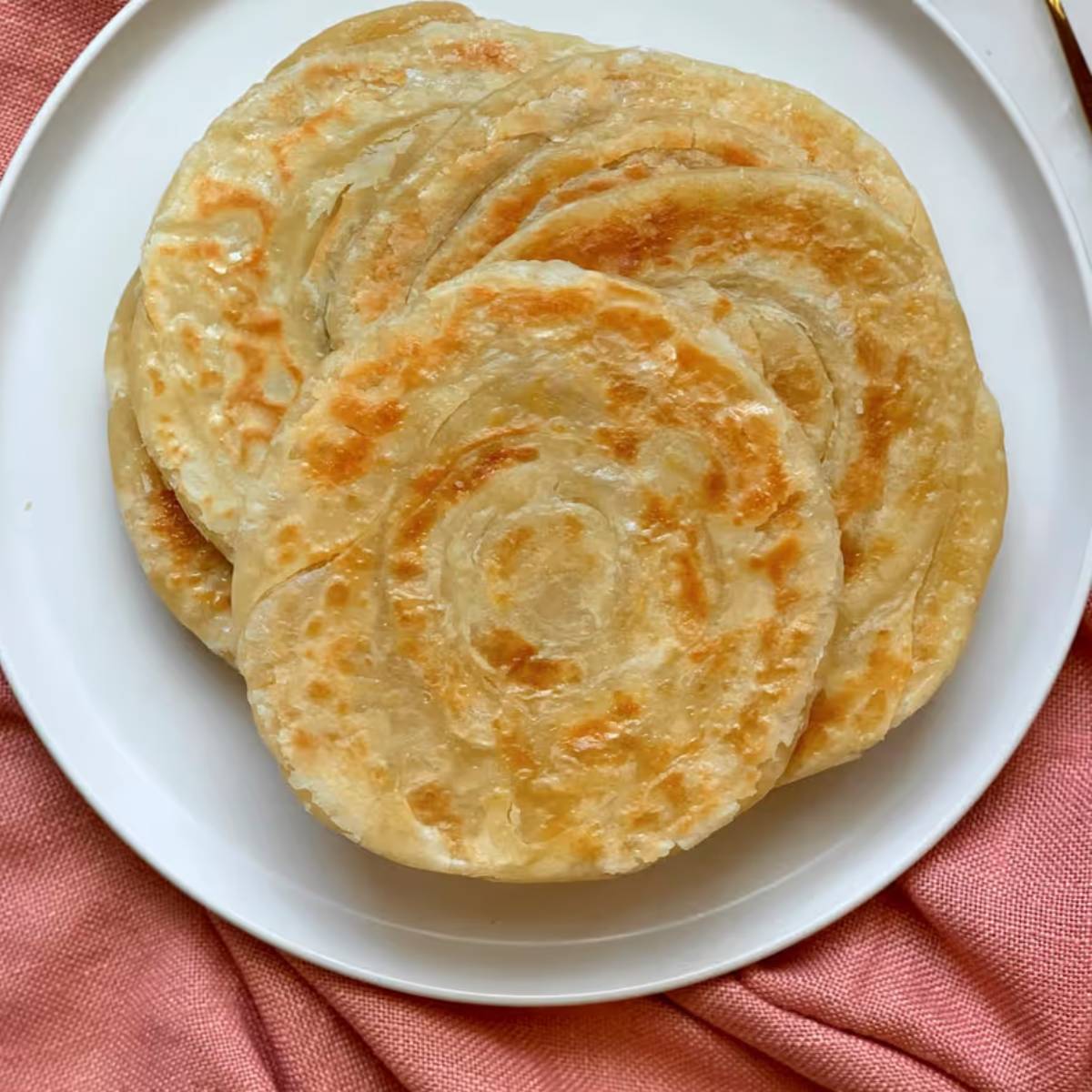 এই পর্যায়ে তাওয়ার ওপর থাকা পরোটার চারধারে সামান্য জল ছড়িয়ে দিন এবং দ্রুত একটি ঢাকনা দিয়ে ঢেকে দিন। জলের বাষ্পের কারণেই পরোটাটি ফুলে উঠবে এবং ভেতর থেকে একদম সেদ্ধ হয়ে নরম হয়ে যাবে। এই সময় গ্যাসের আঁচ মাঝারি রাখতে হবে যাতে পরোটা পুড়ে না যায় বা কাঁ