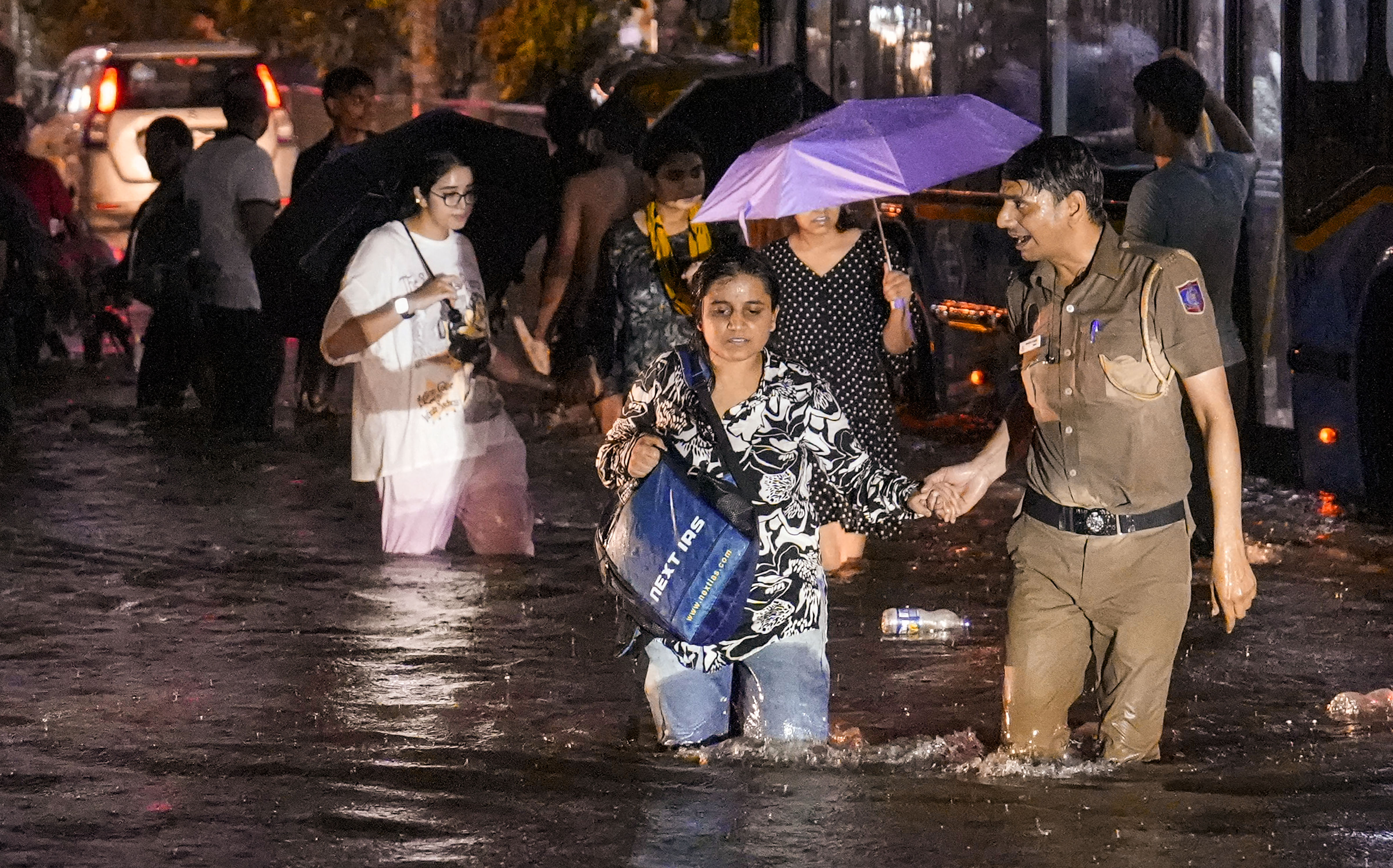 A woman being assisted by a police official while wading through a waterlogged road during rain near (PTI Photo)