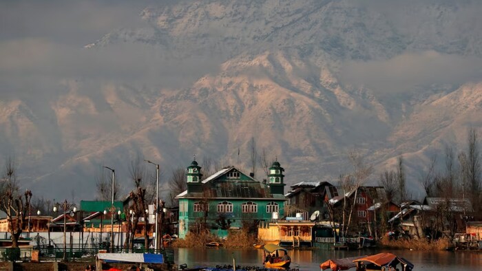 People row their boats in the waters of Dal Lake with the backdrop of snow-covered mountains after a snowfall in Srinagar. (Photo: Reuters)