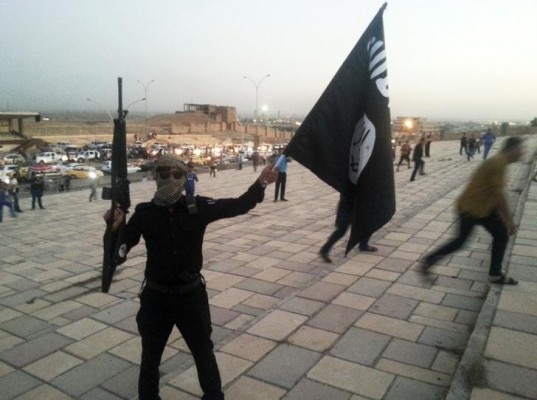 A fighter of the ISIL holds a flag and a weapon on a street in Mosul