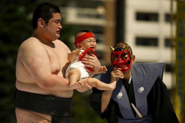 Ring assistant wears mask to scare baby held by amateur sumo wrestler during baby crying contest at Sensoji temple in Tokyo