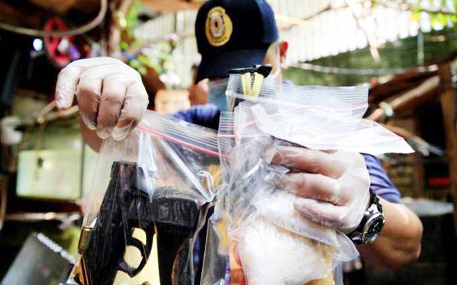 A member of the Philippine National Police (PNP) investigation unit shows confiscated methamphetamine along with illegal firearms seized from suspected drug pushers (Photo: REUTERS)
